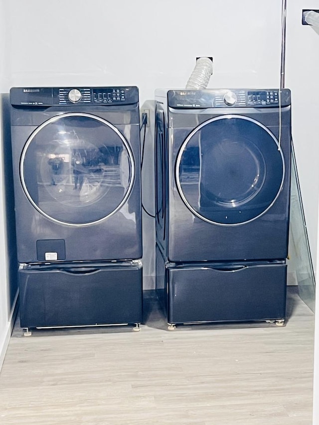 clothes washing area with washing machine and clothes dryer, laundry area, and wood finished floors