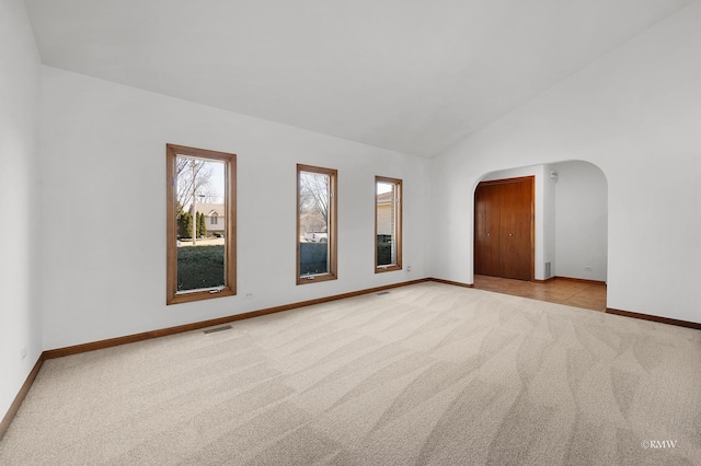 empty room featuring arched walkways, visible vents, light colored carpet, and baseboards