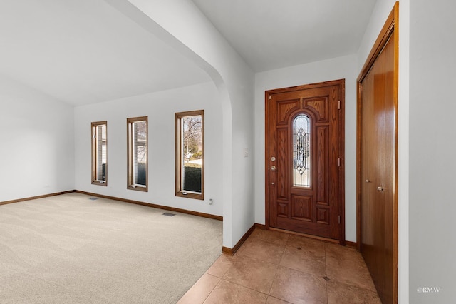 entrance foyer with visible vents, light carpet, arched walkways, light tile patterned flooring, and baseboards