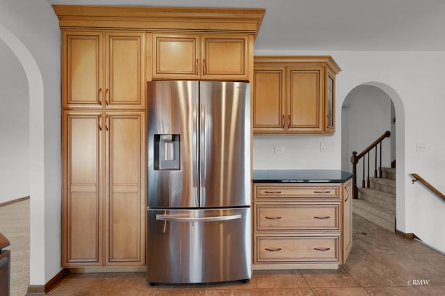 kitchen featuring dark countertops, brown cabinetry, baseboards, arched walkways, and stainless steel fridge