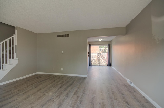 empty room featuring stairway, wood finished floors, visible vents, and baseboards