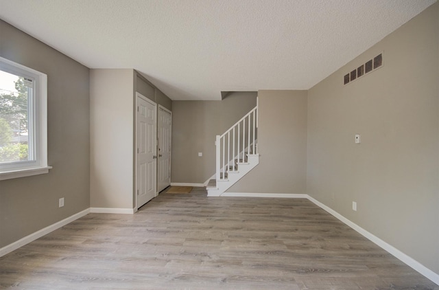 unfurnished room featuring visible vents, baseboards, stairway, light wood-style floors, and a textured ceiling