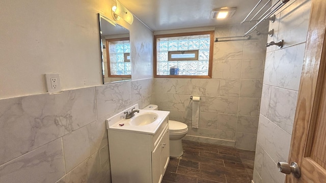 bathroom featuring toilet, tile walls, wainscoting, a shower, and vanity