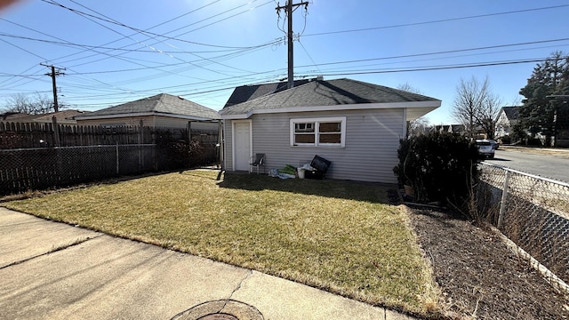 view of side of home featuring a fenced backyard, an outbuilding, a yard, and roof with shingles