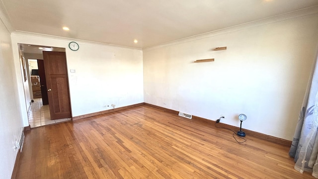 spare room with visible vents, baseboards, wood finished floors, and ornamental molding