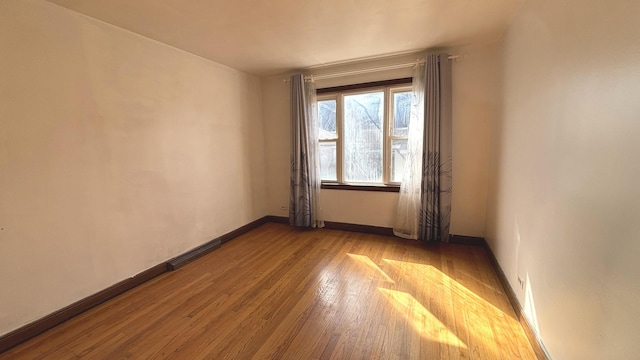 empty room featuring visible vents, baseboards, and hardwood / wood-style flooring