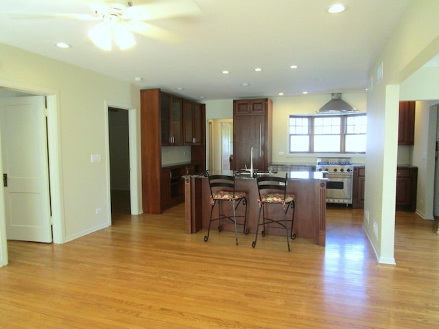 kitchen with dark countertops, high quality appliances, a kitchen bar, an island with sink, and light wood-style flooring