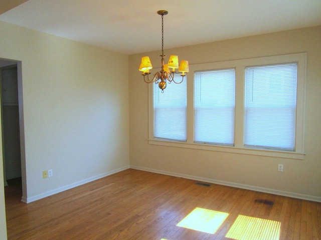 unfurnished room featuring a chandelier, baseboards, and wood finished floors