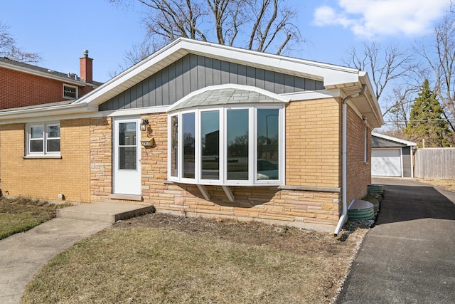 view of front of house with brick siding, board and batten siding, a garage, an outdoor structure, and stone siding