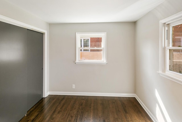 unfurnished bedroom with dark wood finished floors, baseboards, and a closet