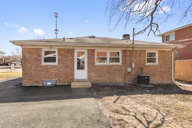 rear view of house with brick siding, entry steps, central AC, and roof with shingles