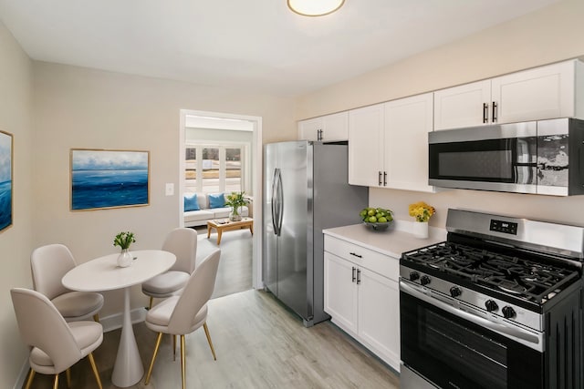 kitchen with baseboards, light countertops, light wood-style flooring, stainless steel appliances, and white cabinetry