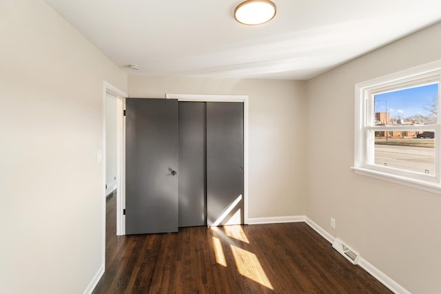 unfurnished bedroom with wood finished floors, baseboards, visible vents, and a closet