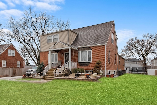 view of front of home featuring brick siding, fence, a front yard, and roof with shingles