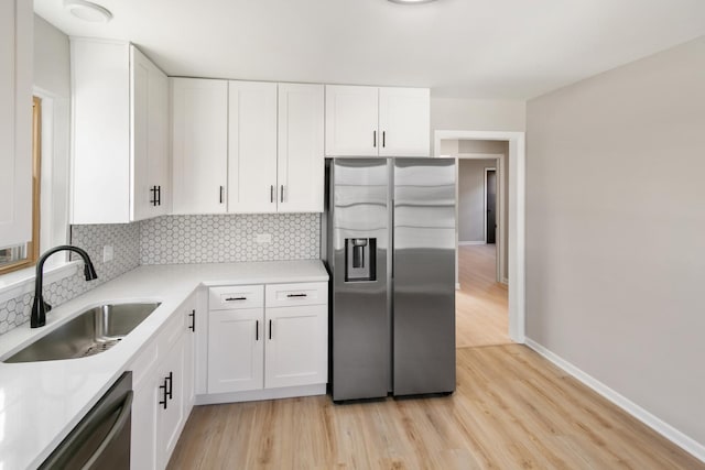 kitchen featuring a sink, appliances with stainless steel finishes, white cabinets, light countertops, and decorative backsplash