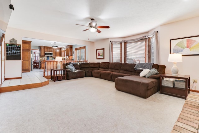 living area featuring light colored carpet, baseboards, and a ceiling fan