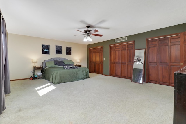 carpeted bedroom featuring a ceiling fan, visible vents, two closets, and baseboards