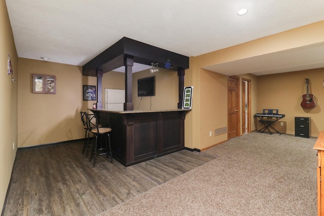 bar featuring wood finished floors, baseboards, carpet floors, freestanding refrigerator, and a bar