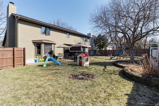 rear view of property with a lawn, a fenced backyard, a chimney, and a playground