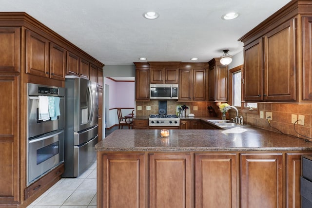 kitchen featuring decorative backsplash, a peninsula, light tile patterned flooring, stainless steel appliances, and a sink