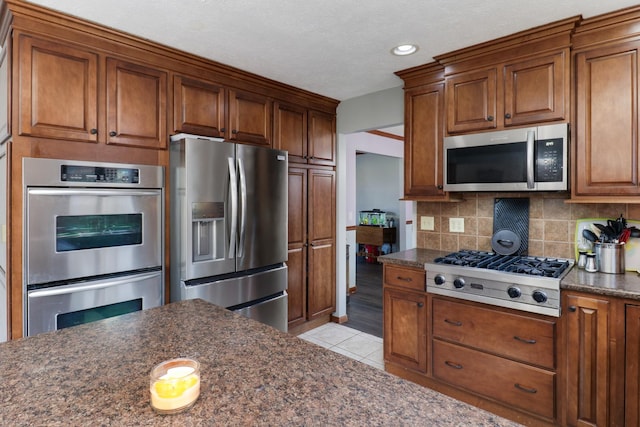 kitchen with tasteful backsplash, stainless steel appliances, brown cabinetry, and light tile patterned flooring