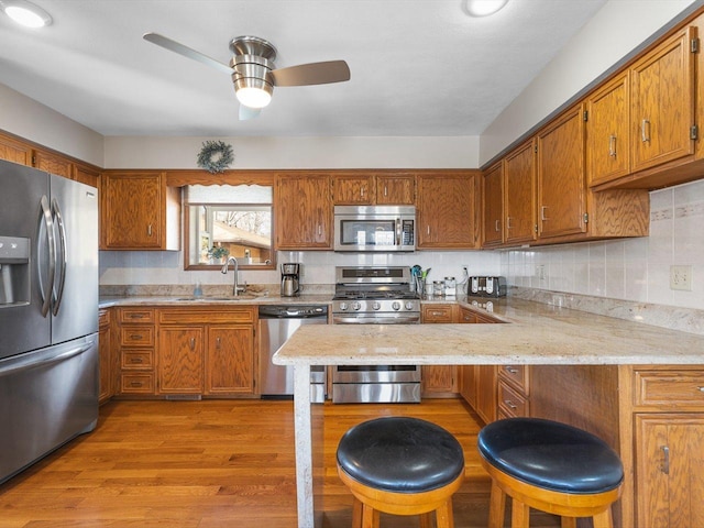 kitchen featuring a peninsula, brown cabinetry, appliances with stainless steel finishes, and a sink