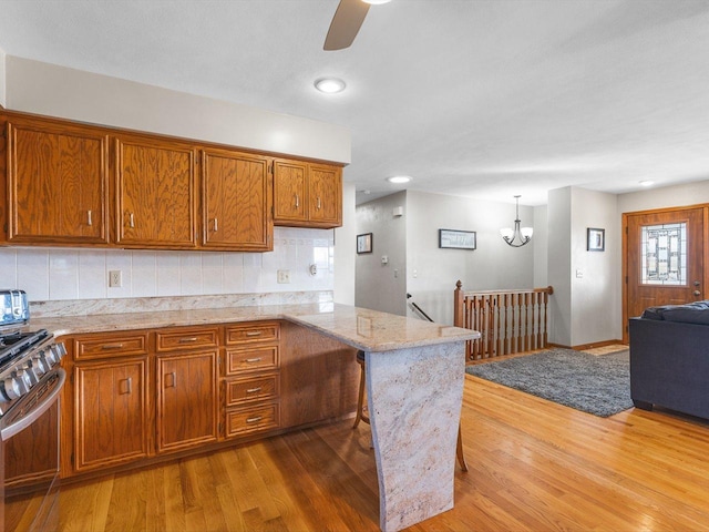 kitchen featuring brown cabinetry, gas range, a peninsula, and wood finished floors