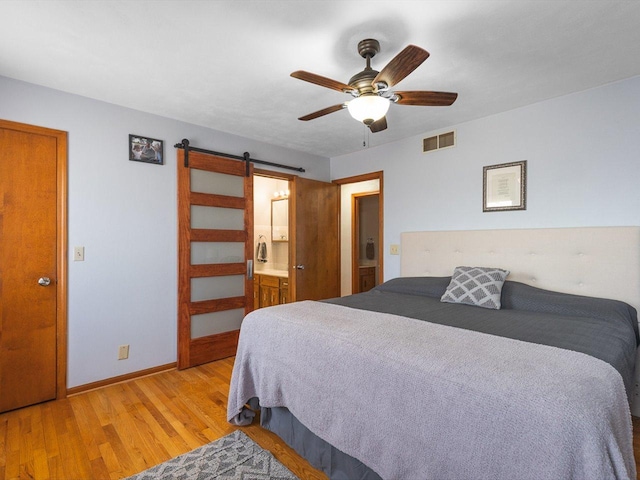 bedroom featuring visible vents, ensuite bathroom, wood finished floors, a barn door, and baseboards