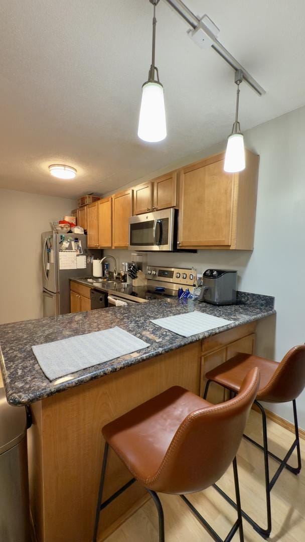 kitchen with baseboards, pendant lighting, a kitchen breakfast bar, appliances with stainless steel finishes, and a peninsula