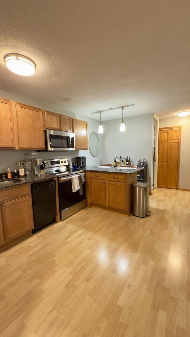 kitchen featuring a peninsula, light wood-style flooring, stainless steel appliances, hanging light fixtures, and a textured ceiling