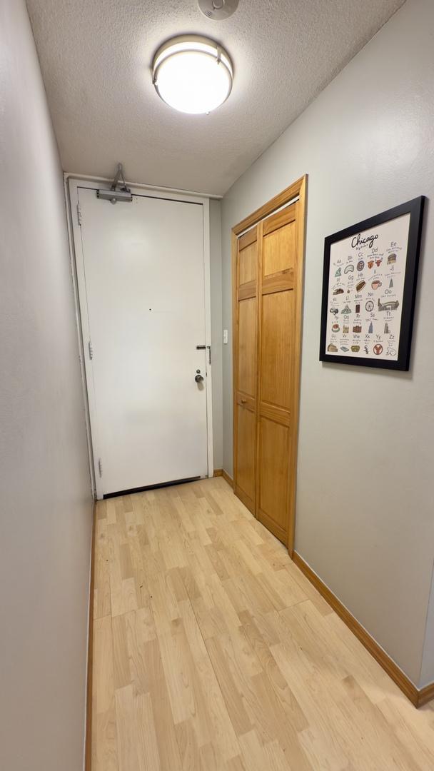 hallway featuring baseboards, a textured ceiling, and light wood finished floors