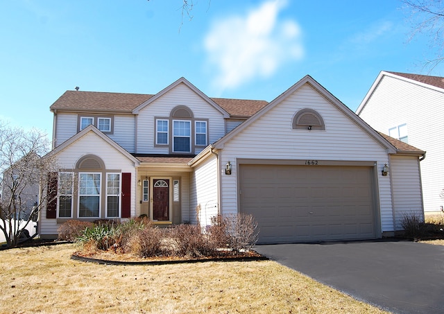 traditional-style house featuring aphalt driveway, an attached garage, a front lawn, and roof with shingles