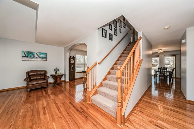 staircase with baseboards, arched walkways, and wood finished floors