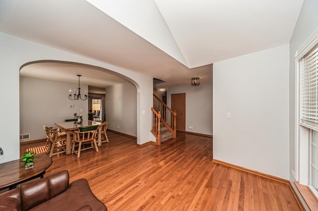 living area with light wood-style flooring, stairway, arched walkways, an inviting chandelier, and vaulted ceiling
