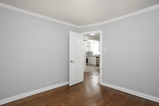 spare room featuring a sink, baseboards, dark wood-style flooring, and ornamental molding