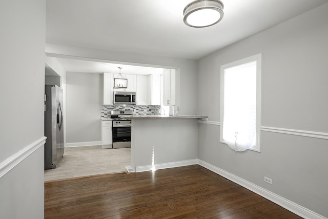 kitchen with decorative light fixtures, light wood-type flooring, decorative backsplash, white cabinets, and stainless steel appliances