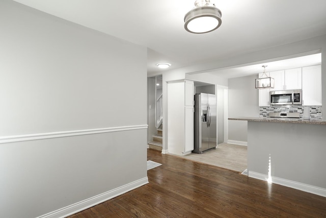 kitchen featuring backsplash, baseboards, light wood-type flooring, appliances with stainless steel finishes, and white cabinetry