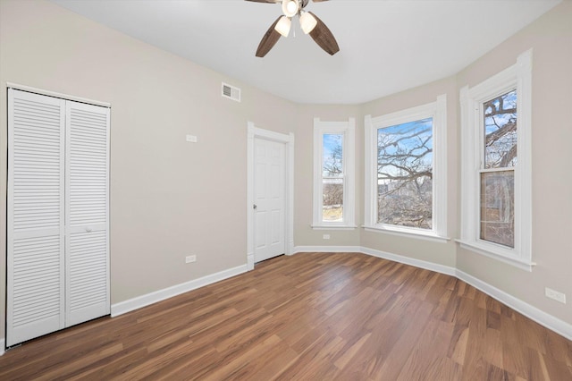 unfurnished bedroom with multiple windows, wood finished floors, visible vents, and baseboards