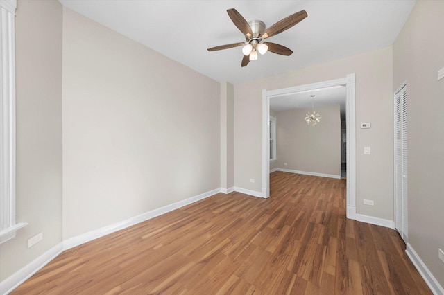 spare room featuring baseboards, wood finished floors, and ceiling fan with notable chandelier