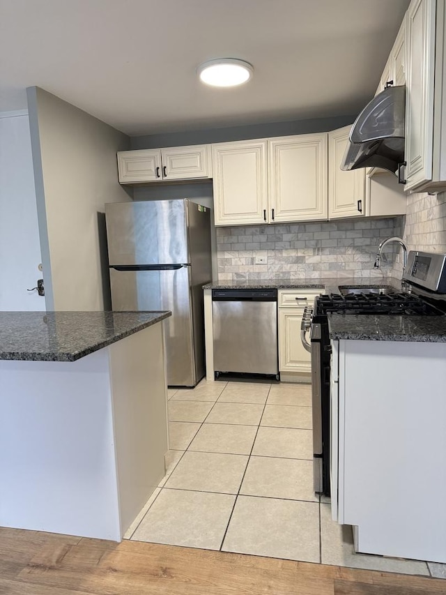 kitchen with ventilation hood, light tile patterned flooring, decorative backsplash, white cabinets, and appliances with stainless steel finishes