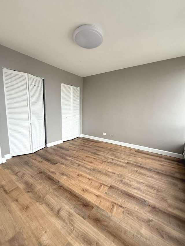 unfurnished bedroom with two closets, baseboards, and wood finished floors