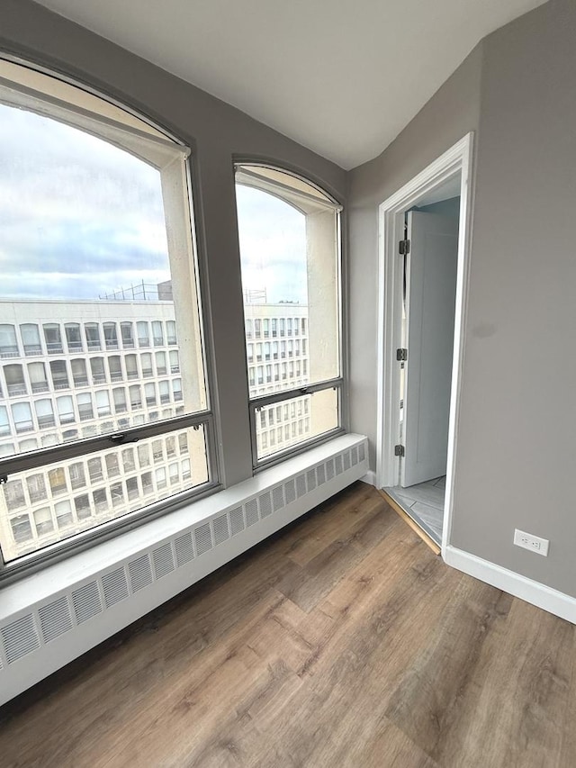 unfurnished room featuring radiator, wood finished floors, and baseboards