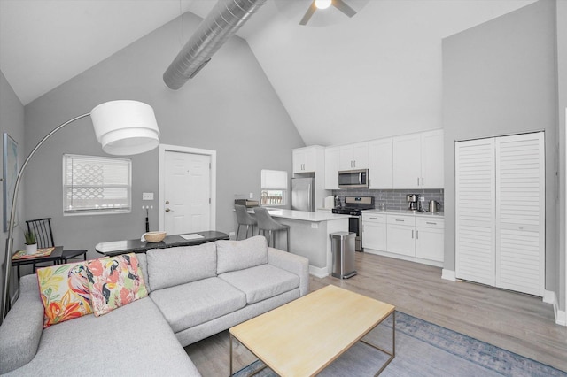 living area with high vaulted ceiling, light wood-style floors, and ceiling fan