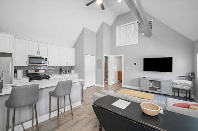 kitchen with a kitchen bar, open floor plan, white cabinetry, stainless steel appliances, and light countertops