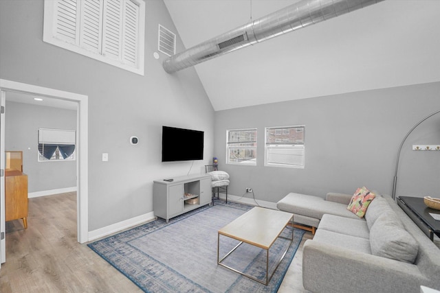 living area featuring wood finished floors, visible vents, a towering ceiling, and baseboards