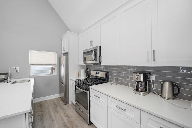 kitchen with a sink, backsplash, white cabinetry, appliances with stainless steel finishes, and lofted ceiling