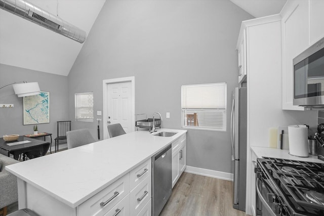 kitchen with light wood finished floors, high vaulted ceiling, a sink, white cabinets, and appliances with stainless steel finishes