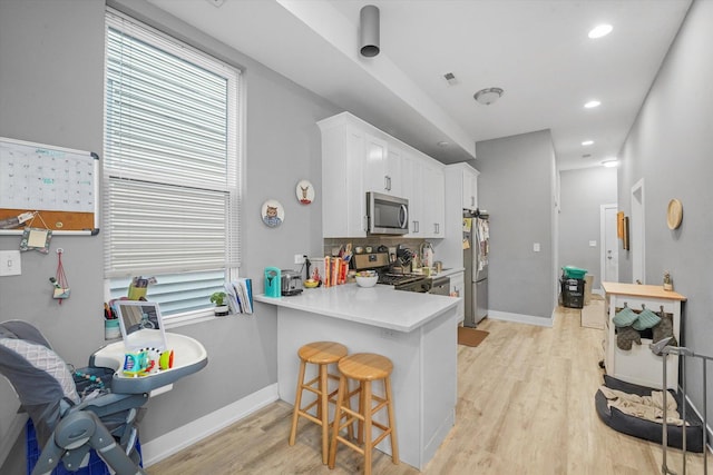 kitchen featuring white cabinetry, a breakfast bar area, light wood-style floors, and appliances with stainless steel finishes