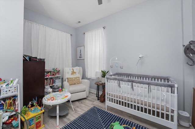 bedroom with visible vents, baseboards, a nursery area, and wood finished floors