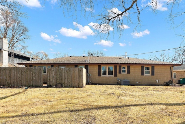 rear view of property featuring brick siding, central AC, a lawn, and fence